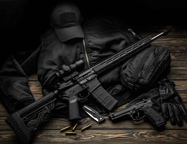 现代自动步枪 在黑暗的背景上有远视瞄准镜 手套放在木制桌子上 卫兵或雇佣兵的制服 — 图库照片