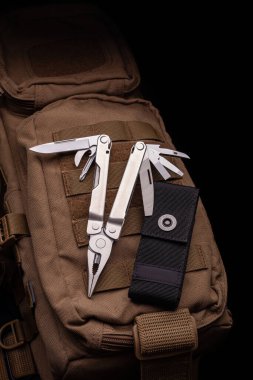 Birçok aletli modern çoklu araç. Taşınabilir çoklu görev aracı çöl rengi bir askeri sırt çantasında yatıyor..