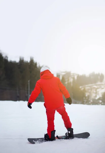 スノーボードのある赤いジャケットの男が山の中腹に立っている — ストック写真