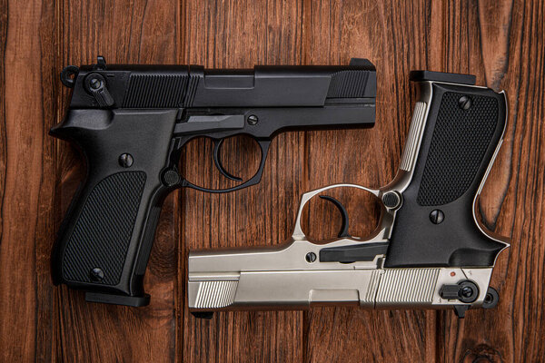 Two guns. Short-barreled weapons in black and silver. Weapons for self-defense. Two pistols on a wooden background.