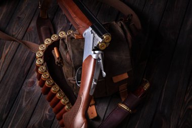 Üzerinde fişekler ve deri bir çantada bıçak olan, tahta arka planda duran bir av tüfeği. Avlanma kavramı