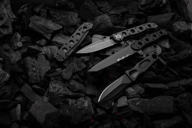 Modern knives with black blades. Hunting, military and folding knives on smoldering charcoal. Black background.