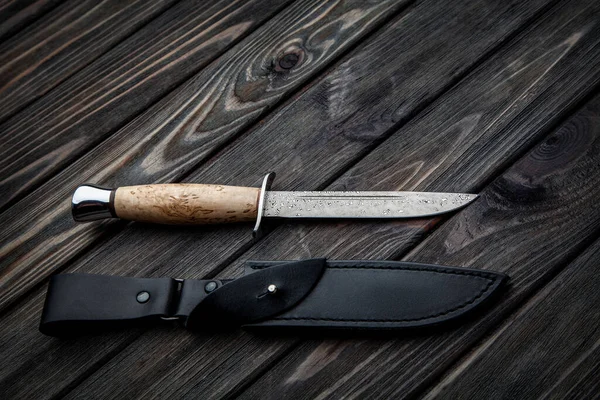 木製のハンドルと黒い革の鞘を持つ狩猟ナイフ ダマスカス鋼刃 板からのヴィンテージ木製の背景 — ストック写真