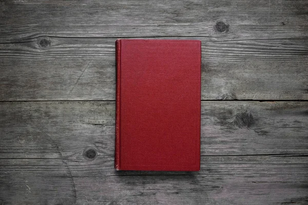 A closed book on an old wooden table. Red hard cover. Vintage background.