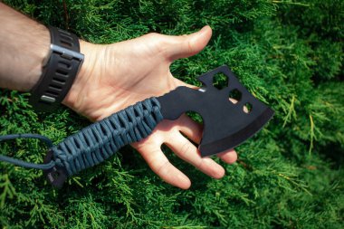 A small black ax with a paracord-wrapped handle. A tool for cutting branches or firewood in the forest. Self defense weapon. Green background.