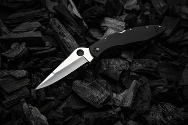 Modern knife with a silver blade. Hunting, military folding knife on smoldering charcoal. Black background.