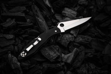 Modern knife with a silver blade. Hunting, military folding knife on smoldering charcoal. Black background.