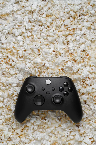 Black gamepad on popcorn background. Game poster or postcard concept. Rest for the game and popcorn.
