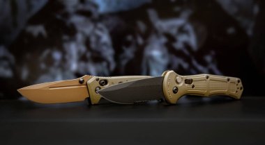 Khaki military pocket folding knives. Compact metal sharp knife with a folding blade. Blurred background.