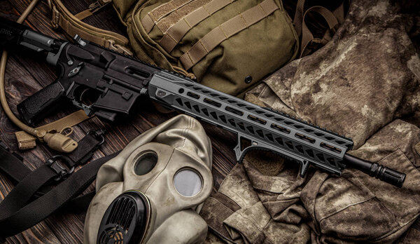 Современный автоматический карабин, рюкзак и противогаз на деревянном столе. Набор истребителей, готовых к любым боевым условиям.