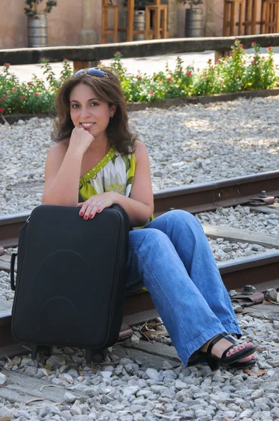 Young traveling woman sitting with suitcase along the train trac — Stock Photo, Image