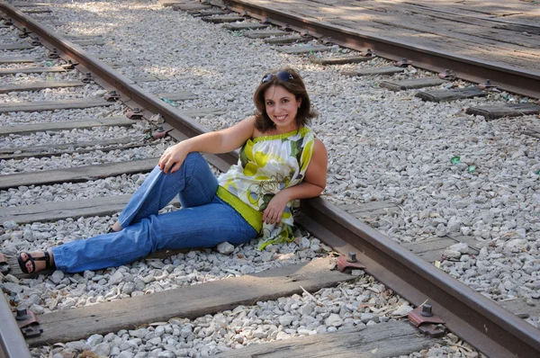 Молодая путешествующая женщина сидит с чемоданом вдоль железнодорожного пути — стоковое фото