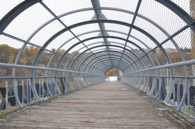 Ahşap yolu olan metal tünel köprüsü. Her iki tarafında ahşap yürüyüş yolu ve yuvarlak zemin ışıkları olan tünel şeklinde metal çubuklar köprü..