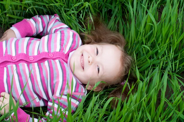 Улыбающаяся маленькая девочка лежит на зеленой траве — стоковое фото