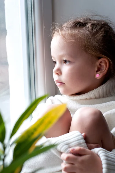 Liten flicka ser från fönstret — Stockfoto