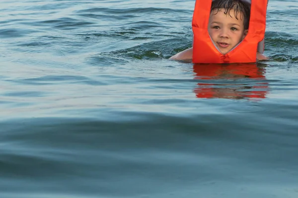 ライフジャケットの助けを借りて海の水の上に5歳の男の子が保持されます — ストック写真