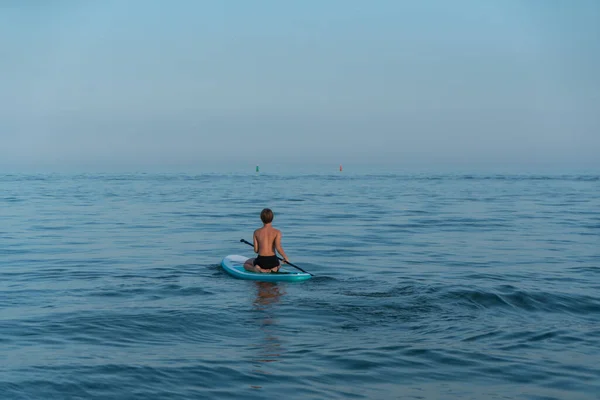 Een jongen van 11 jaar oud zwemt op een SUP board in de zee na zonsondergang. — Stockfoto