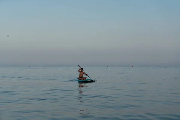 A boy of 11 years old swims on a SUP board in the sea after sunset. — Stock Photo, Image