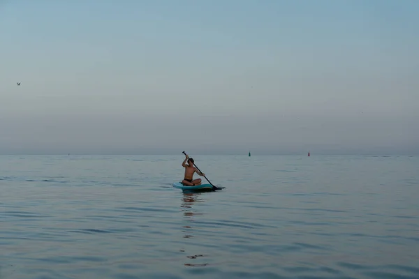 Een jongen van 11 jaar oud zwemt op een SUP board in de zee na zonsondergang. — Stockfoto