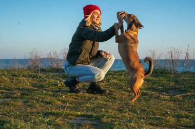 A blonde girl with a purebred dog from the shelter. Playing with a dog on the seashore. Friendship of a dog and a person.