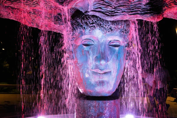 Fountain - a stone face in a Greek park in streams of water at night. — Stok Foto