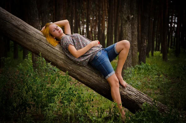 Söt flicka med rött hår på en stock i skogen. — Stockfoto