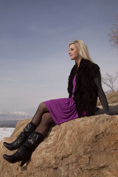 Vrouw paarse rok zitten op rock kant — Stockfoto