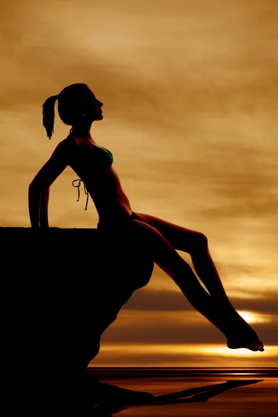 Woman silhouette sitting on rock by water — Stock Photo, Image