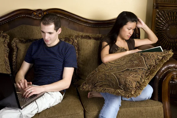 Man and woman sitting on two different ends of couch doing their own things. — Stock Photo, Image