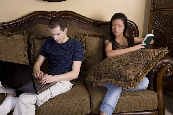 Mann und Frau sitzen an zwei verschiedenen Enden der Couch und tun ihre eigenen Dinge. — Stockfoto