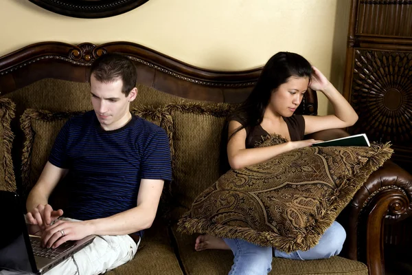 Hombre y mujer sentados en dos extremos diferentes del sofá haciendo sus propias cosas . — Foto de Stock