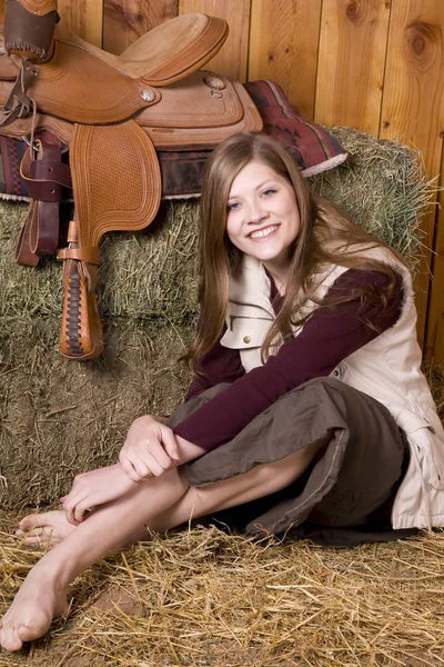 Woman sitting by saddle on hay — Stock Photo, Image