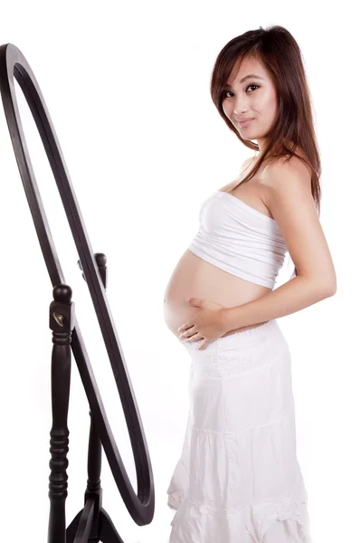 Pregnant woman in white by mirror smiling — Stock Photo, Image