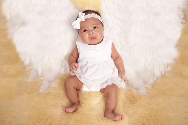 Bebê deitado em um tapete de pele com suas asas de anjo branco — Fotografia de Stock