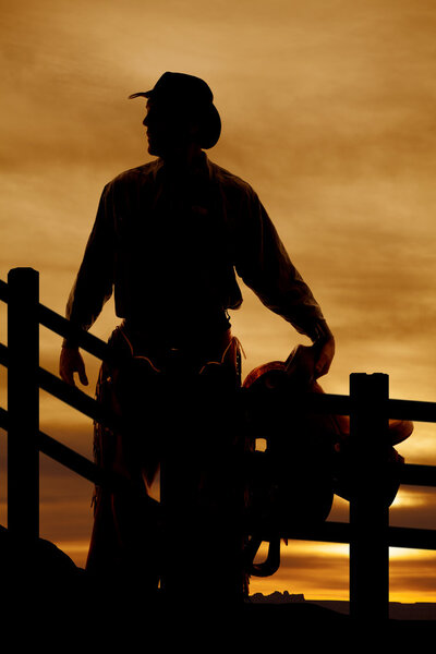 silhouette cowboy saddle in front of fence