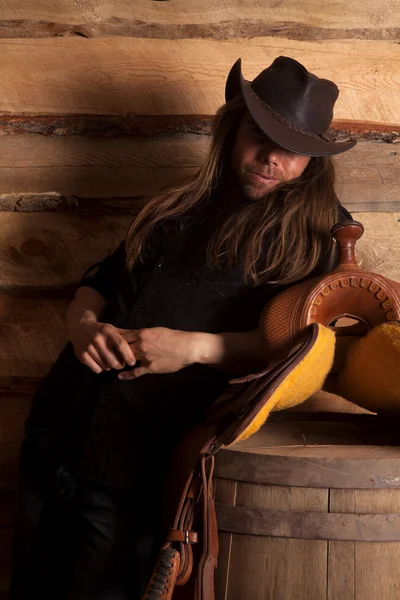 Cowboy in low light by saddle — Stock Photo, Image