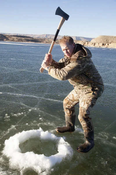 Man in camo chopping hole in ice with axe swing — Stock Photo, Image