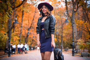 Şehirli arka plan sonbahar portresi üzerinde günlük kıyafetler ve siyah deri ceketli genç moda kadını. Hippi kız sokakta poz veriyor. Zarif sonbahar kıyafetleri içinde modaya uygun uzun saç modeli. şapka.