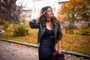 Şehirli arka plan sonbahar portresi üzerinde günlük kıyafetler ve siyah deri ceketli genç moda kadını. Hippi kız sokakta poz veriyor. Zarif sonbahar kıyafetleri içinde modaya uygun uzun saç modeli. şapka.