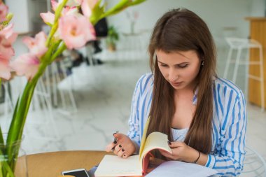 Kafede kahve fincanıyla öğrenirken not defterine konsantre olmuş kız öğrenci. Uzaktan çalışma projesini planlamak için bilgi toplayan dalgın kadın serbest yazar. Çiçekçi.