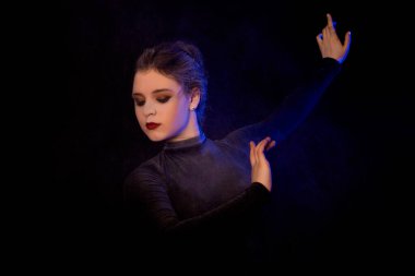 Siyah arka planda dans eden balerin. Çekici balerin, siyah mavi ve mor dumanlı arka planda stüdyoda zarifçe poz veriyor. Sanatçı ve jimnastikçi.