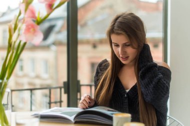 Kafeteryada kitap ya da dergi okuyan beyaz bir kız. Serbest meslek, iş kavramı. Sabah rutini.