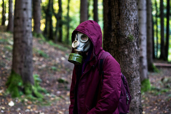 casual young man in a gas mask standing on the forest. Ecological catastrophy. Post apocalyptic survivor in gas mask. Man at forest.
