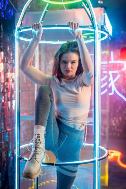 Dans eden genç bir moda kadınının stüdyo portresi. Tarz. Moda mankeni şık kıyafetler içinde renkli neon ışıklı portreler içinde. Stüdyoda pembe ve mor ışık altında modaya uygun giyinen seksi kadın..