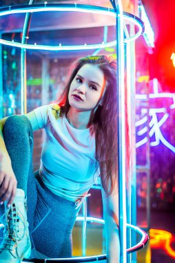 Dans eden genç bir moda kadınının stüdyo portresi. Tarz. Moda mankeni şık kıyafetler içinde renkli neon ışıklı portreler içinde. Stüdyoda pembe ve mor ışık altında modaya uygun giyinen seksi kadın..