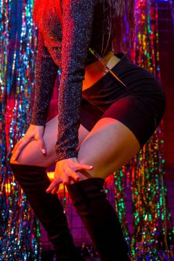 Dans eden genç bir moda kadınının stüdyo portresi. Tarz. Moda mankeni şık kıyafetler içinde renkli neon ışıklı portreler içinde. Stüdyoda pembe ve mor ışık altında modaya uygun giyinen seksi kadın..