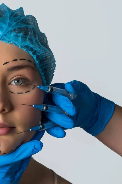 在做面部整形手术时对妇女进行横向拍摄 略带斑纹的女性脸 美容师手持灰色背景的手术器械 — 图库照片