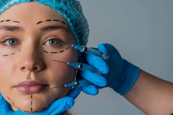 在做面部整形手术时对妇女进行横向拍摄 有斑纹线条的女性脸 美容师手持灰色背景下分离的手术器械 — 图库照片