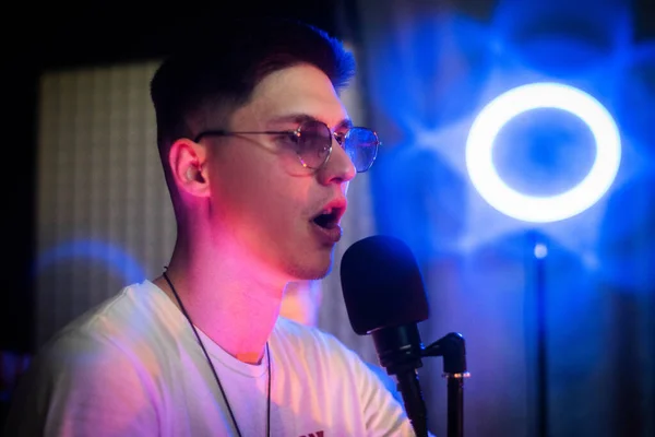 Portrait of handsome young man with sunglasses hosting show live in studio. Close up. Young rapper recording performance. Young emotional expressive performer. Neon.