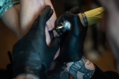 Kuaförde dövmenin kesilip atılmış hali. Profesyonel bir dövme sanatçısı dövme makinesinin iğnesini kullanarak cilde mürekkep yerleştirir. Stüdyoda çalışan profesyonel bir dövmeci..